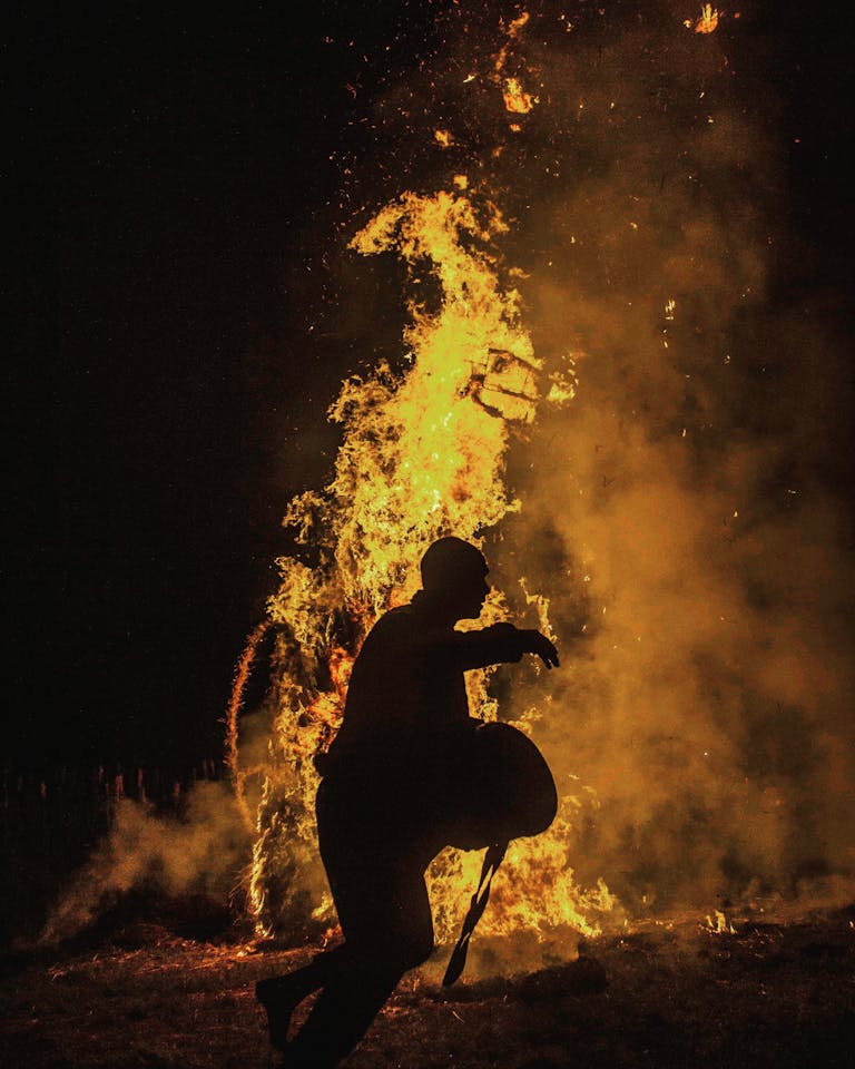 Dramatic silhouette of a man running against the backdrop of a large blazing fire at night.